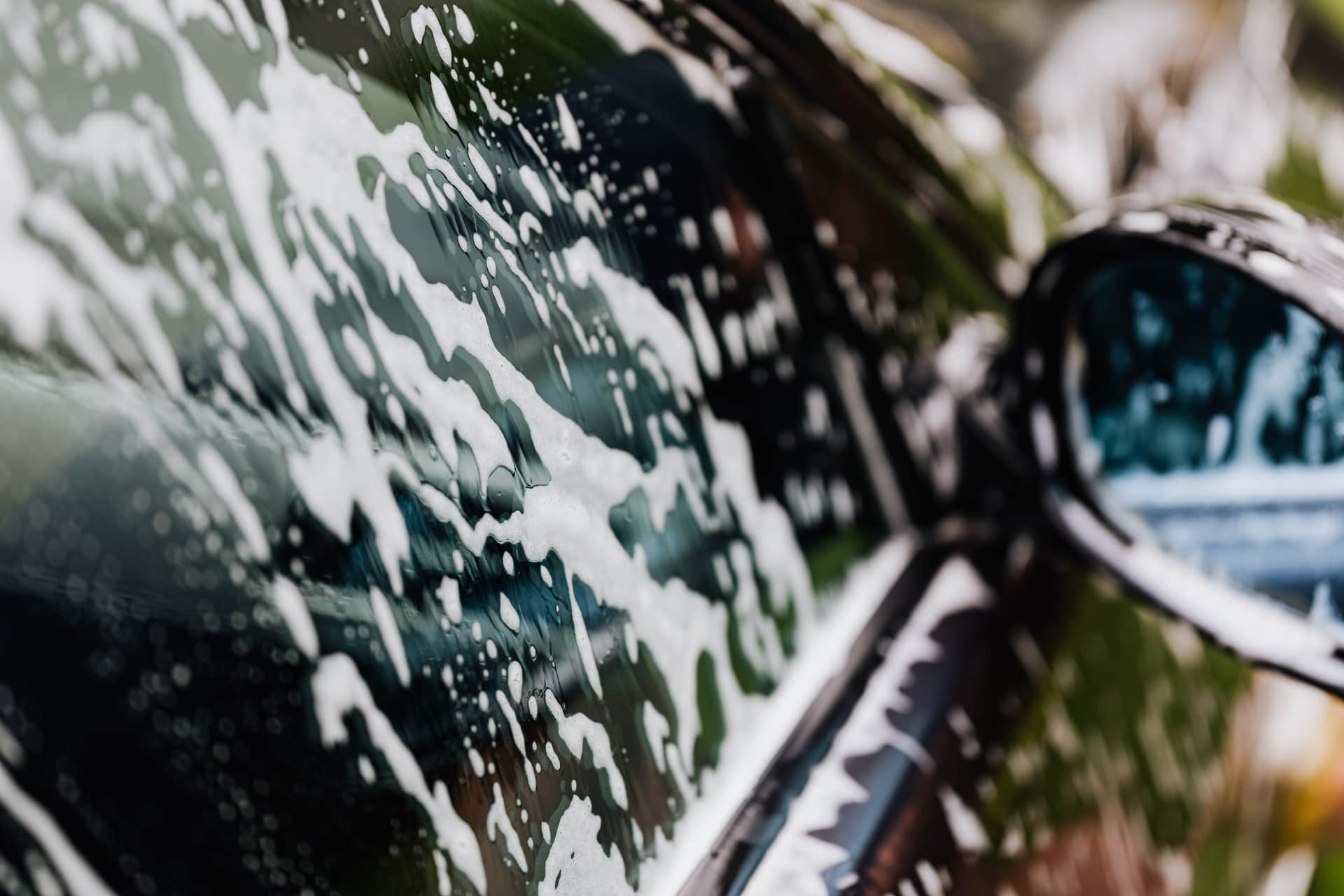 Thick white snow foam clinging to a car's painted panel