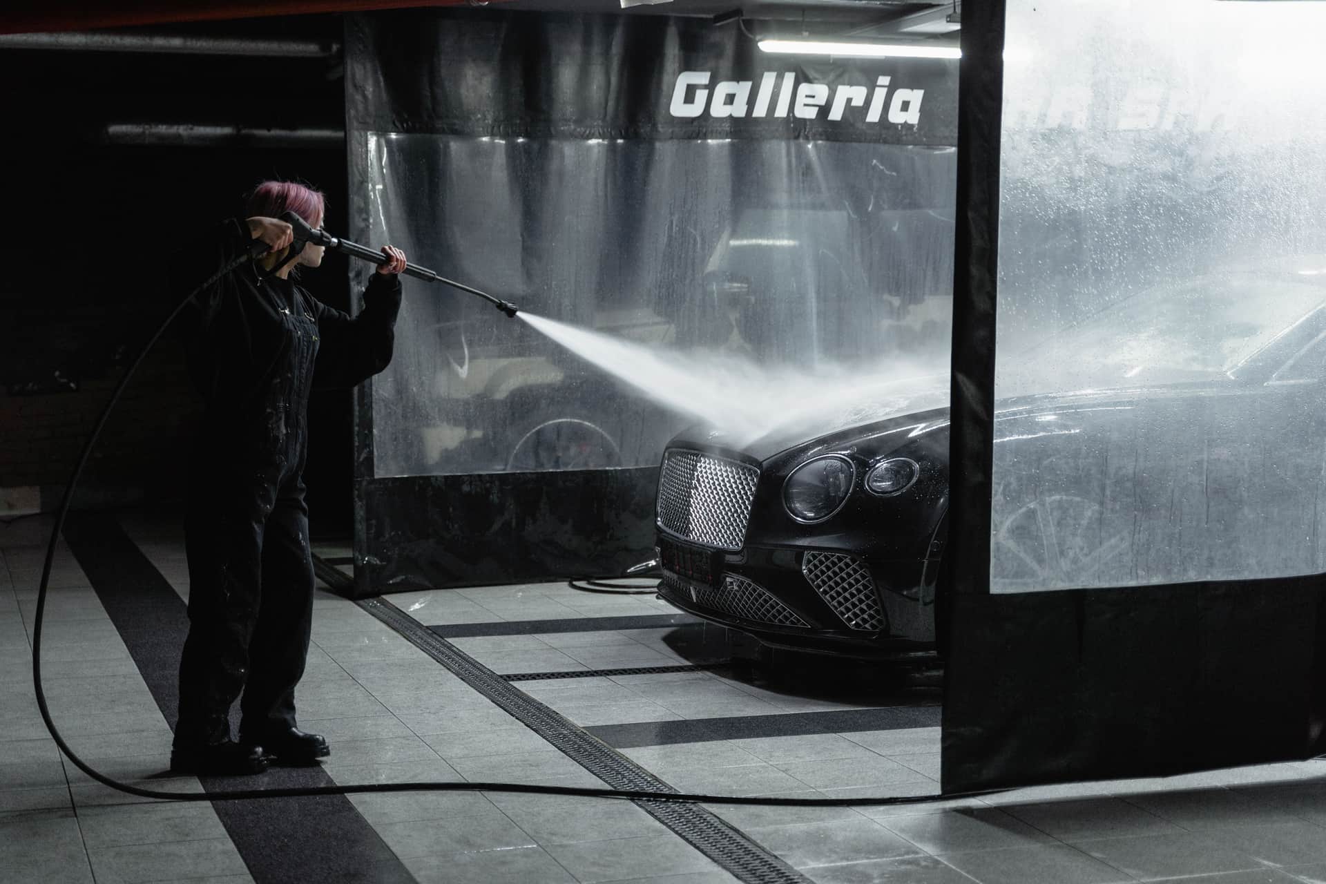 A car being rinsed with a pressure washer under directional light